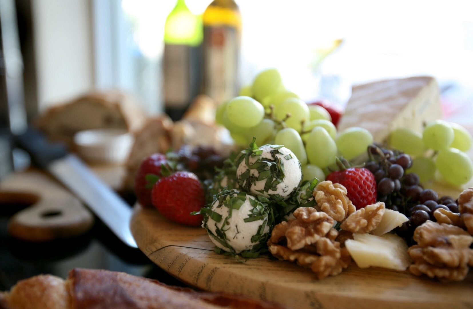 A wooden platter with grapes, cheese and nuts.